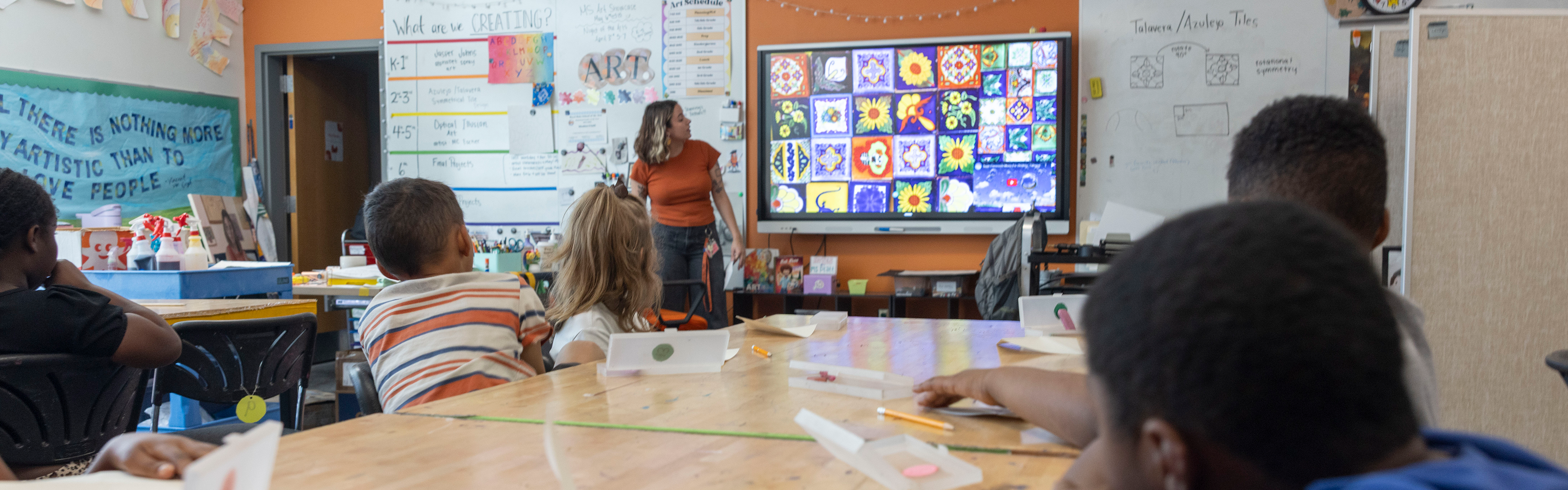 teacher in front of a classroom of kids showing colorful handrawn tile graphics on a screen