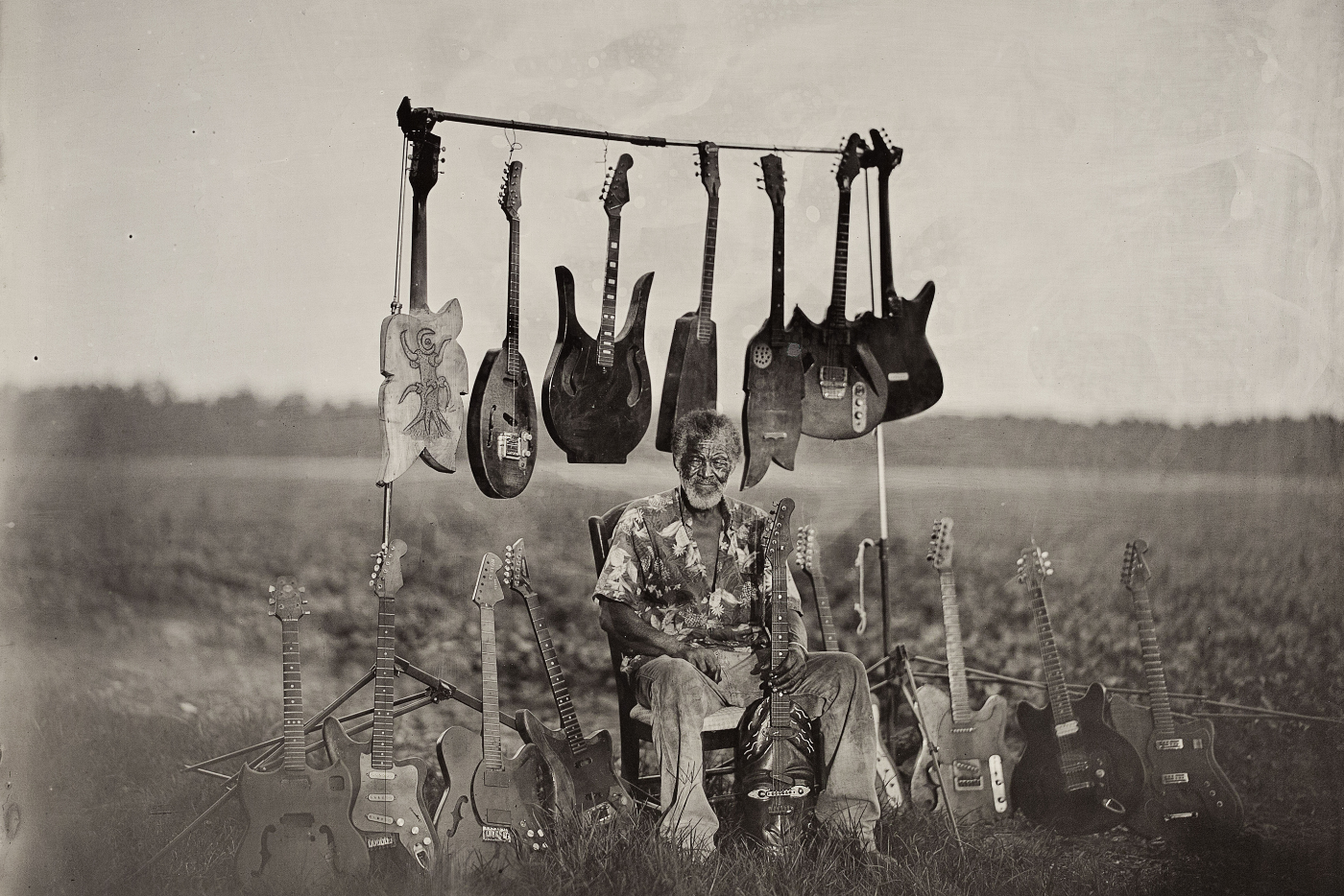 an old black and white photo of musician and guitar maker Freeman vines sitting in a field surrounded by guitars he has built