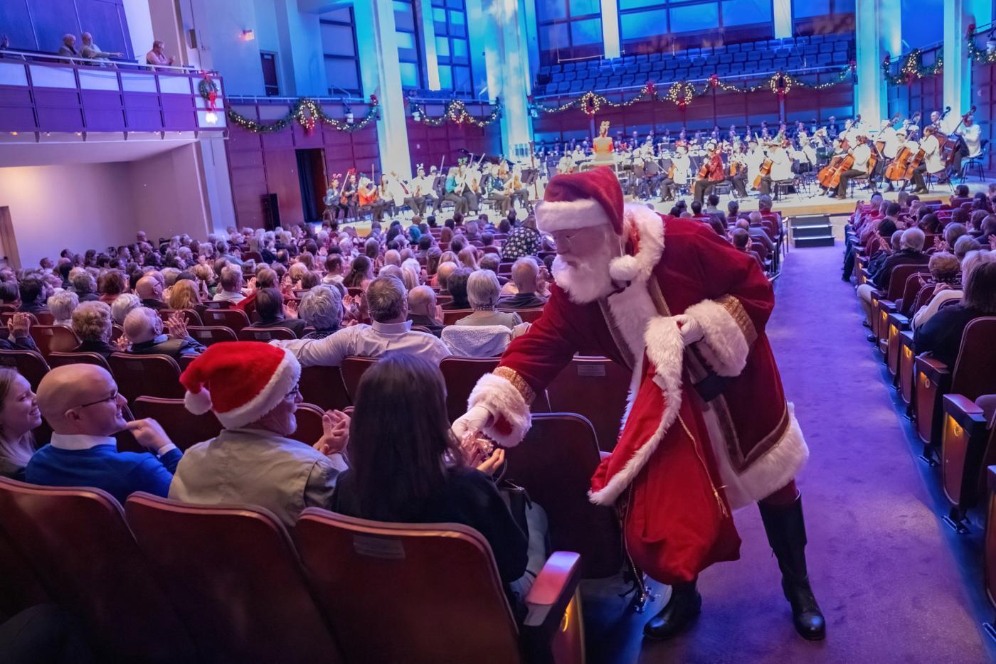 A Santa hands out presents in a filled concert hall