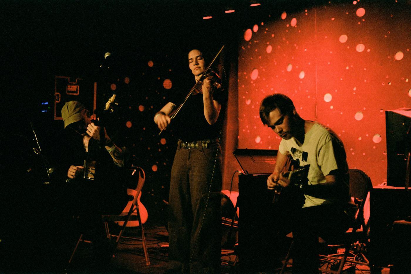 Magic Tuber Stringband plays on a dimly-lit stage with a reddish backdrop