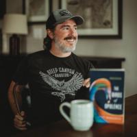 Wiley Cash smiling and sitting at a table with a coffee cup and book