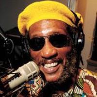 Larry Reni Thomas smiling in front of a microphone wearing a yellow hat