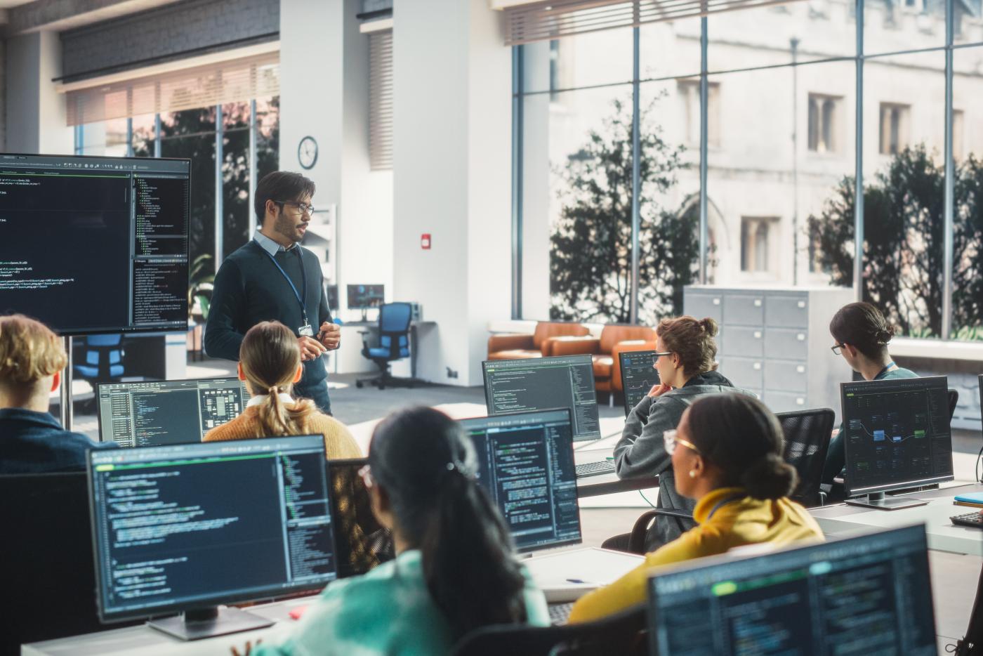 Teacher Giving Computer Science Lecture to Diverse Multiethnic Group of Female and Male Students in a College Room. Projecting Slideshow with Programming Code. Explaining Information Technology