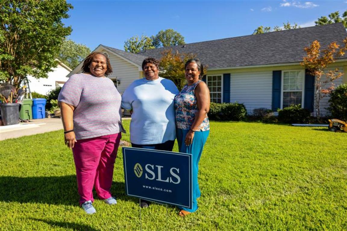 Matalene Waters, her daughter, and goddaughter smiling for a photo in front of Ms. Waters' newly repaired home