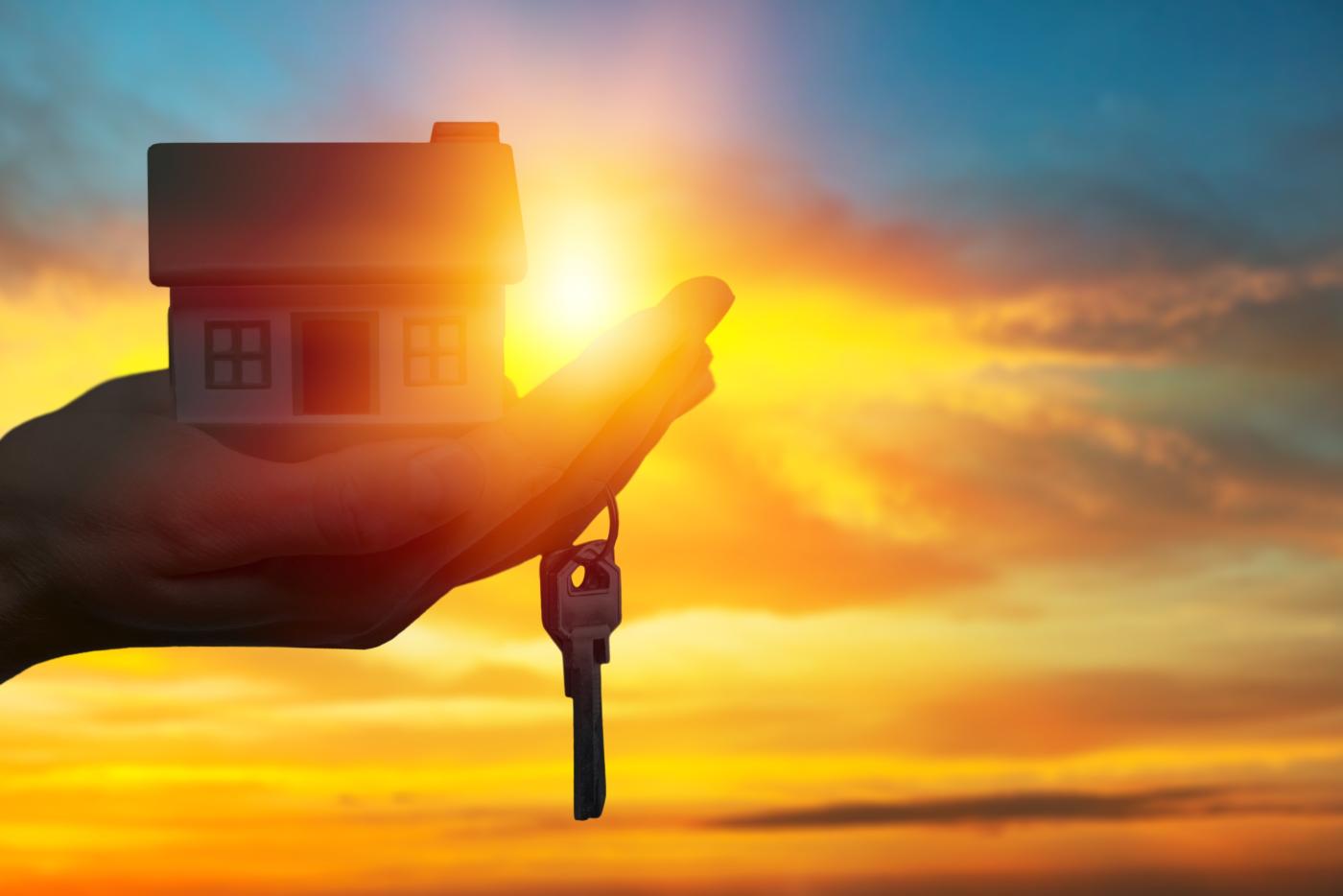 A hand holding a set of keys and a miniature house to signify home ownership