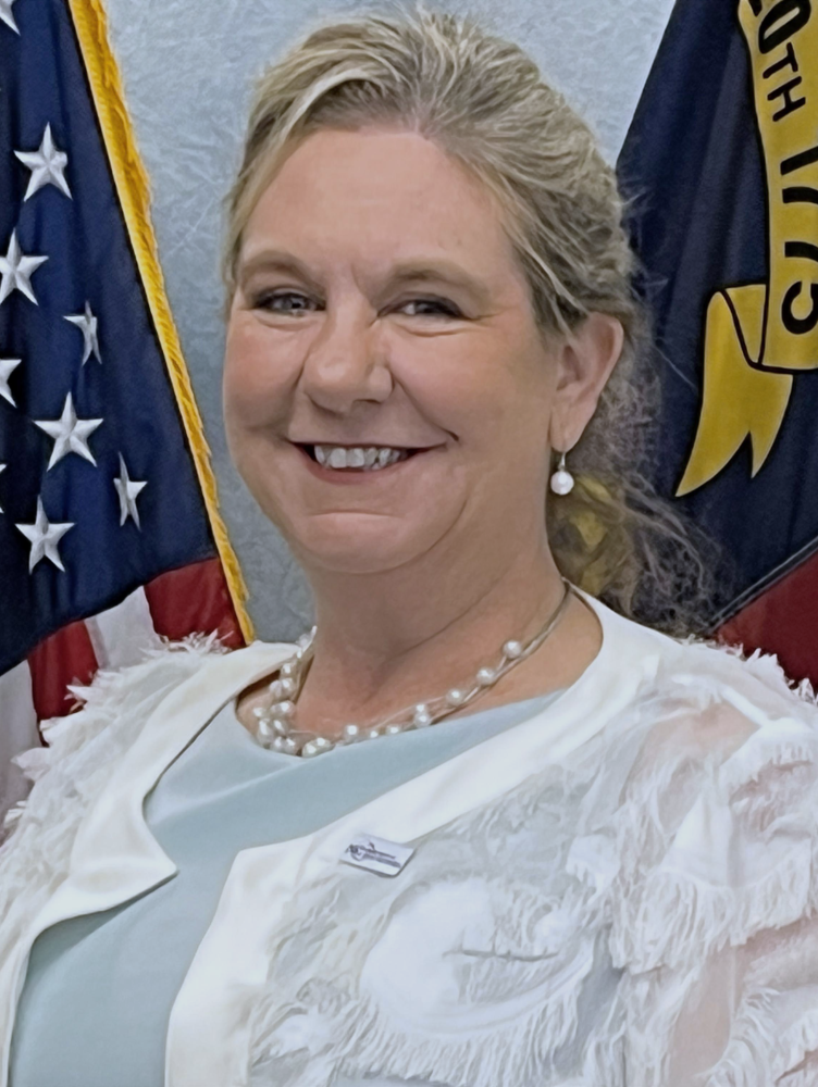 woman in white sweater with pearls in front of flags