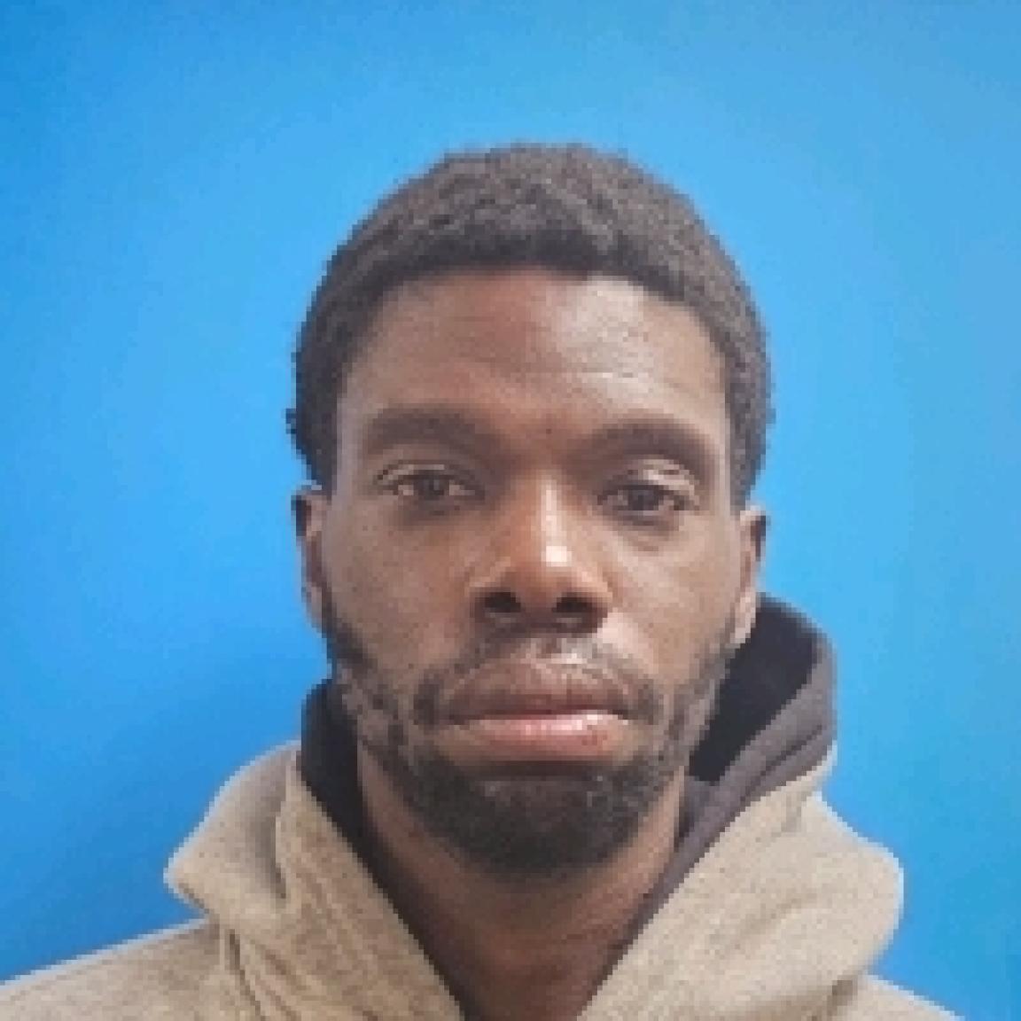 Black man in tan hoodie with short beard and mustache mugshot