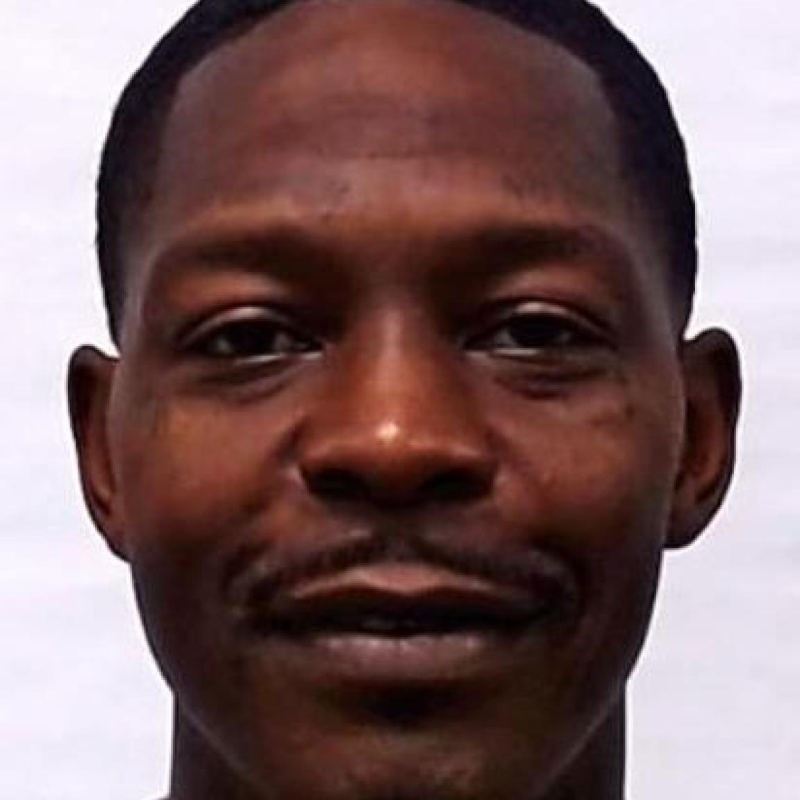 A smiling man with short hair and a goatee against a plain background. 