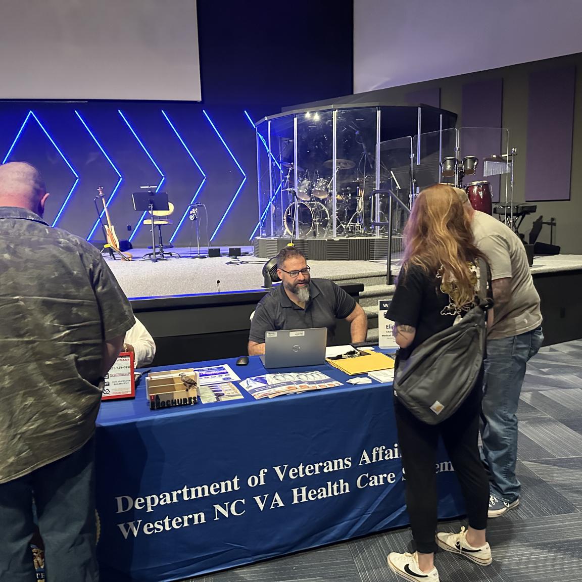 three people looking at materials on a table and talking to two people at the table