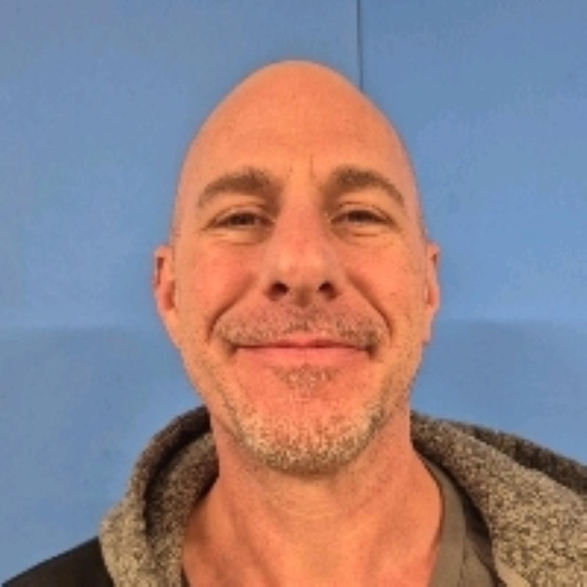 smiling bald man with light stubble wearing a hooded jacket,