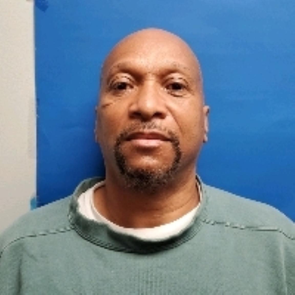 bald Black man with a trimmed goatee wearing a green sweatshirt