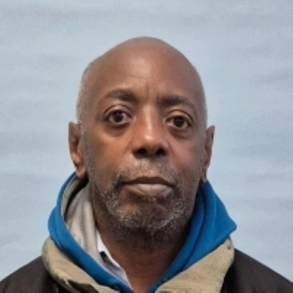 Portrait of a serious-looking bald Black man with a gray beard, wearing a blue hooded jacket 