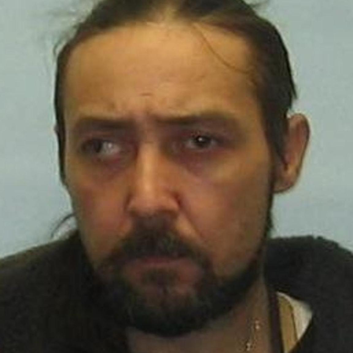  bearded man with long dark hair pulled back, looking sideways with a serious expression