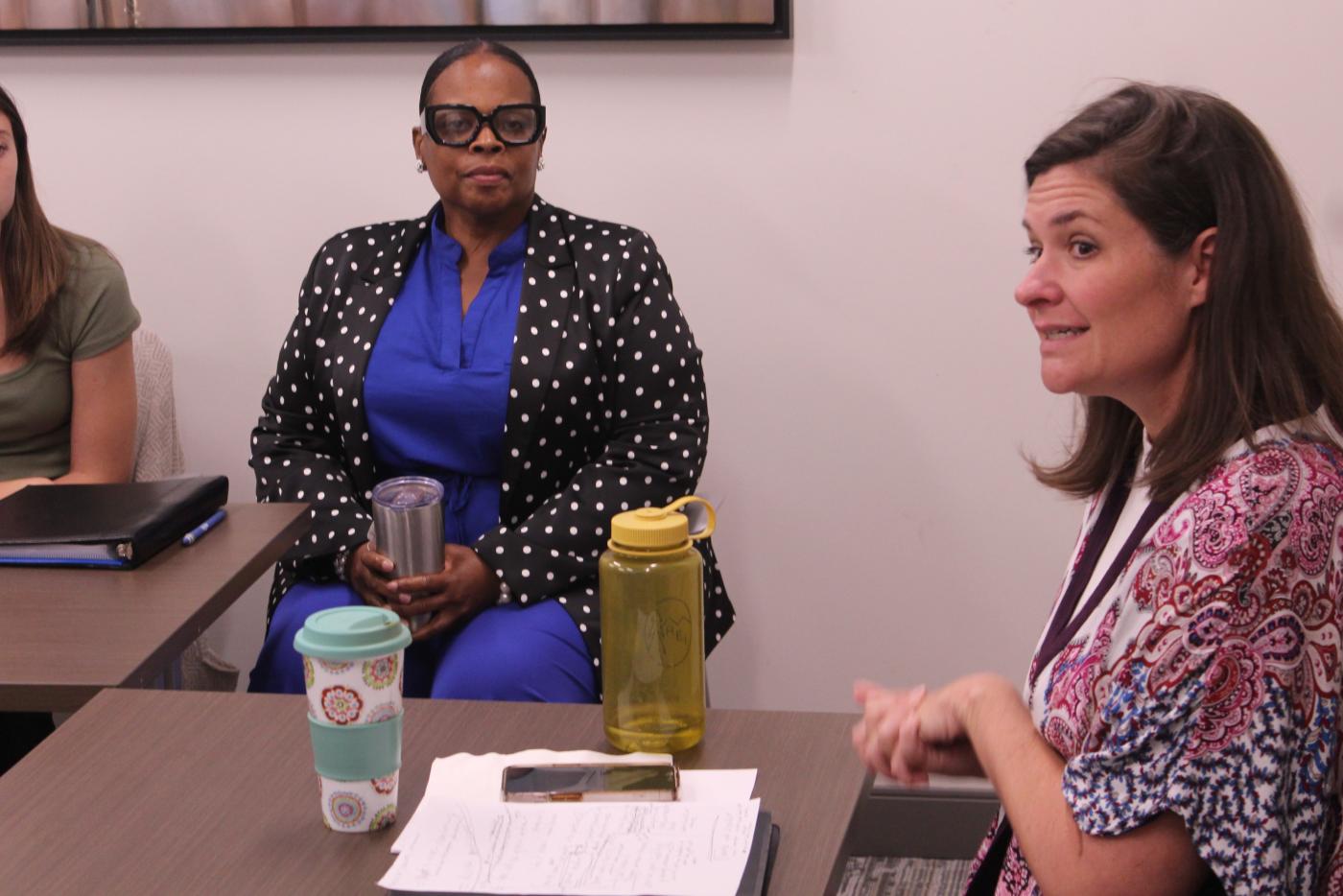 Dr. Sarah Job, dressing in a flowered blouse, speaks with two ladies at a table.