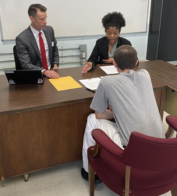 Male offender in gray t-shirt and white pants speaks with a female Duke Student and D.J. Dore, head of the Duke Pro Bono Program.