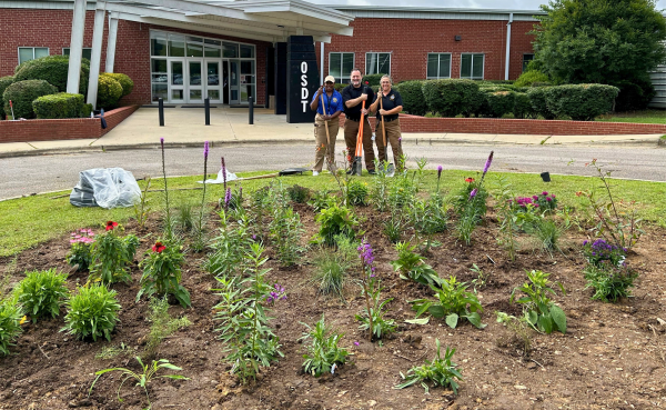Three people stand at freshly planted garden