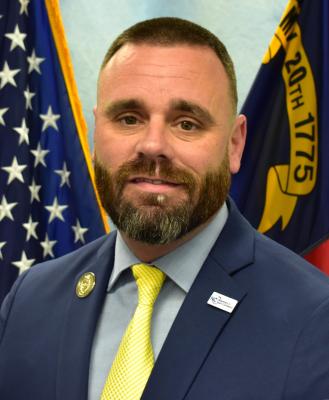 bearded white man in gray jacket, blue shirt, yellow tie