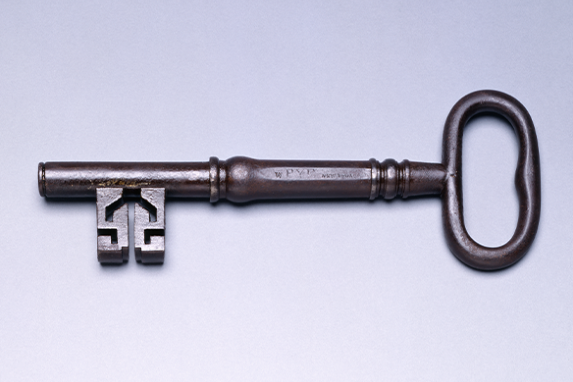 An antique metal key lying horizontally against a light background.