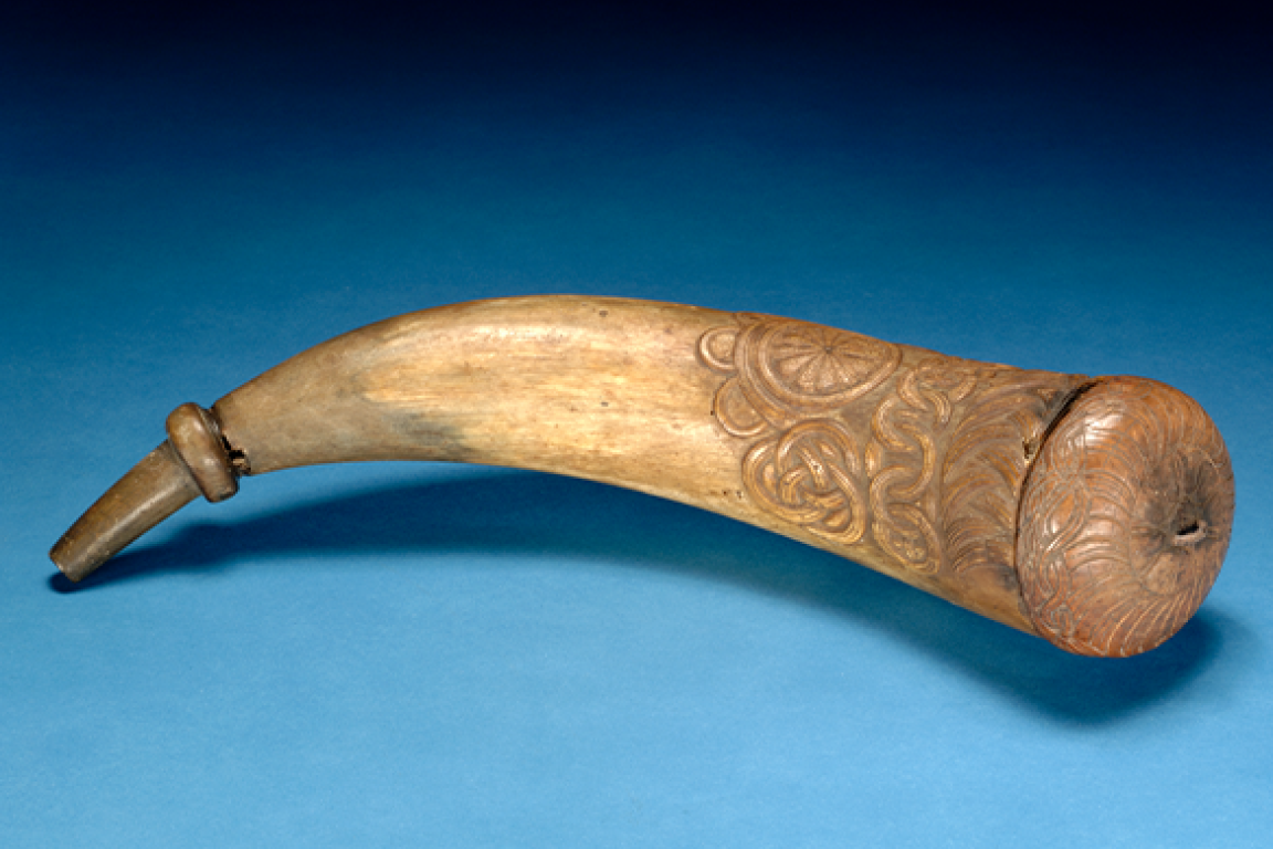 A tan horn with carved decorative patterns and a capped end over a blue background.