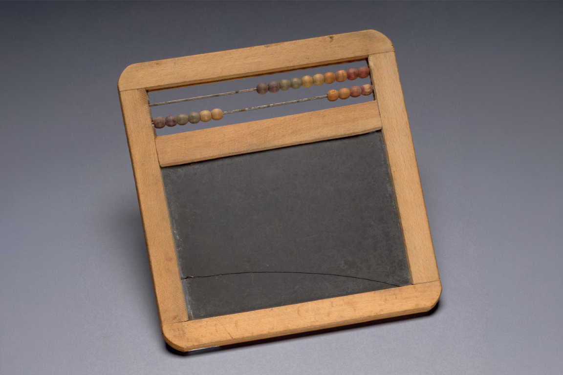 An antique wooden school slate with a built-in abacus at the top, featuring two rows of worn, colorful beads.