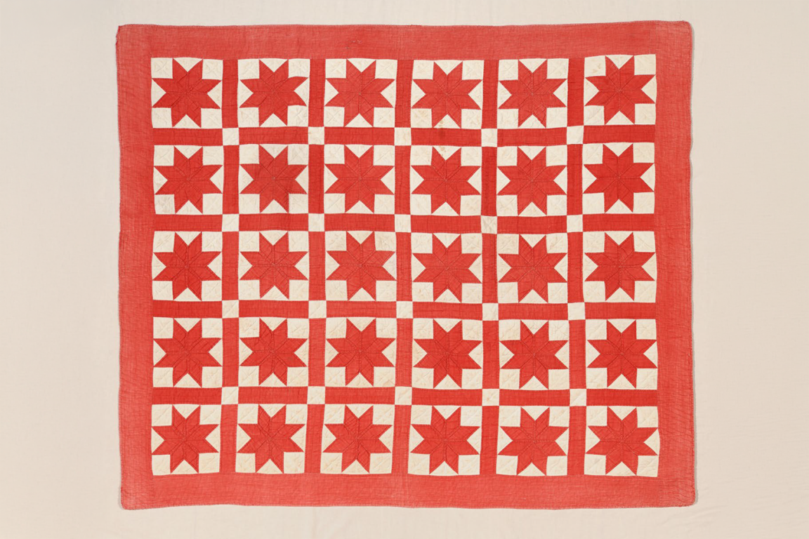 A red and white handmade quilt featuring a grid of 30 eight-pointed stars. One star in the lower-right quadrant is a contrasting tan color, while the rest are red on white squares, all framed by a wide red border.