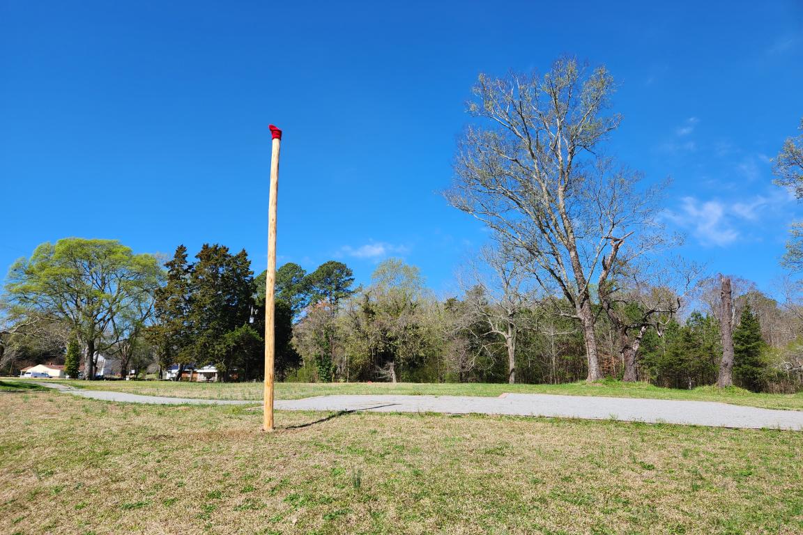 Hand-hewn wooden pole with a red cap standing in a grassy field at Historic Halifax under a clear blue sky.