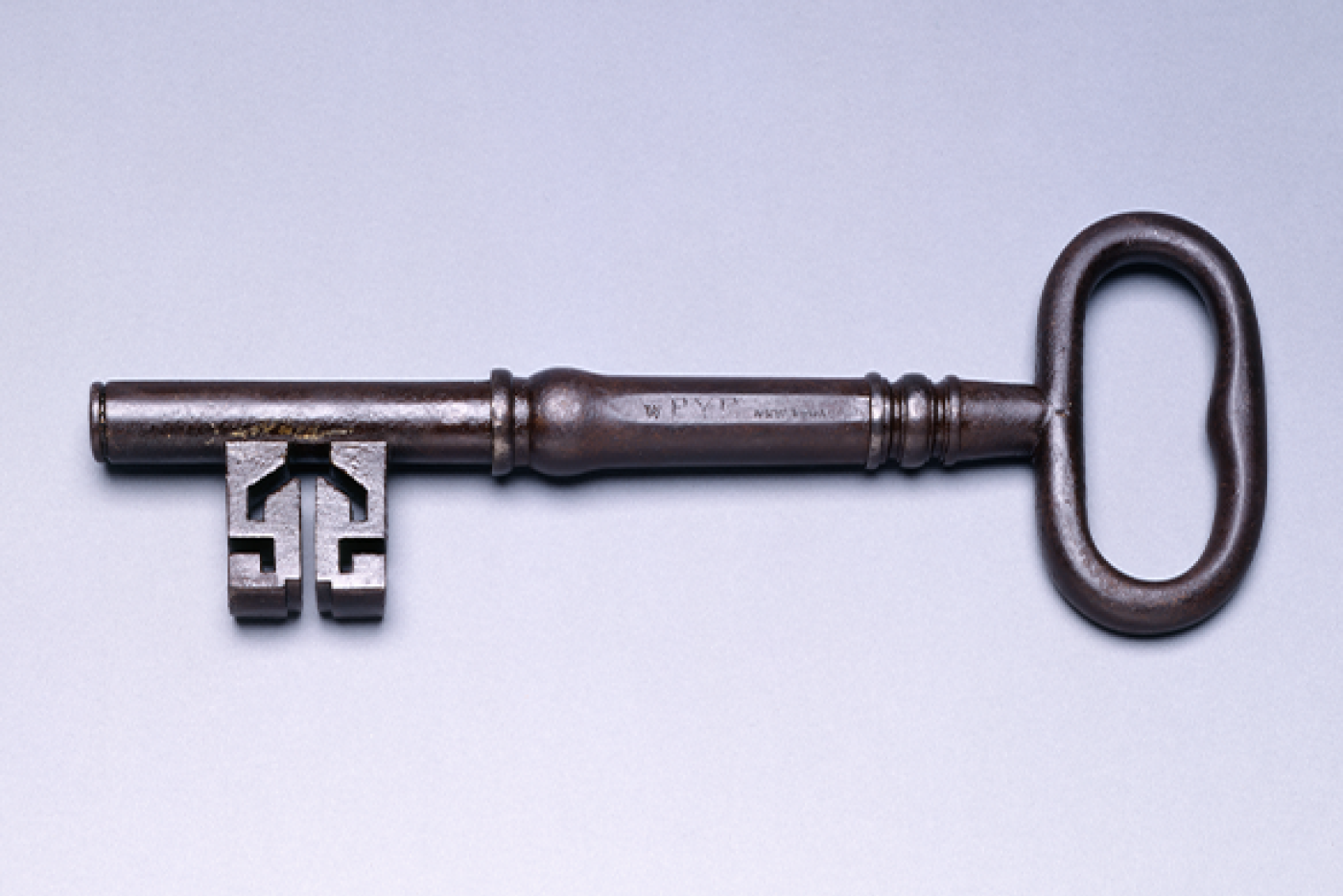 An antique metal key lying horizontally against a light background.