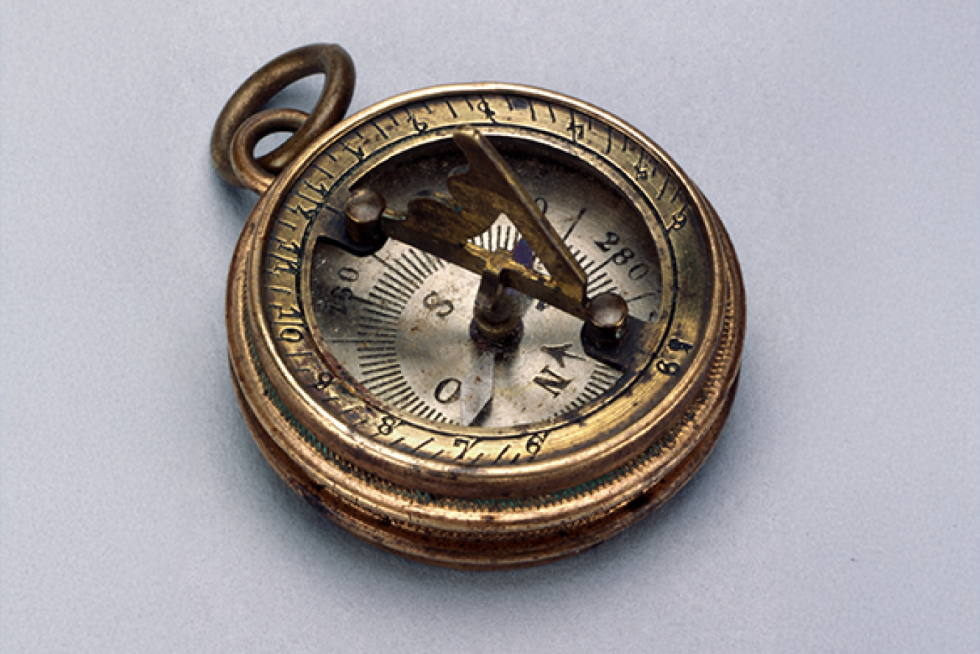 An antique brass compass featuring a sundial raised over the face, photographed over a light background.
