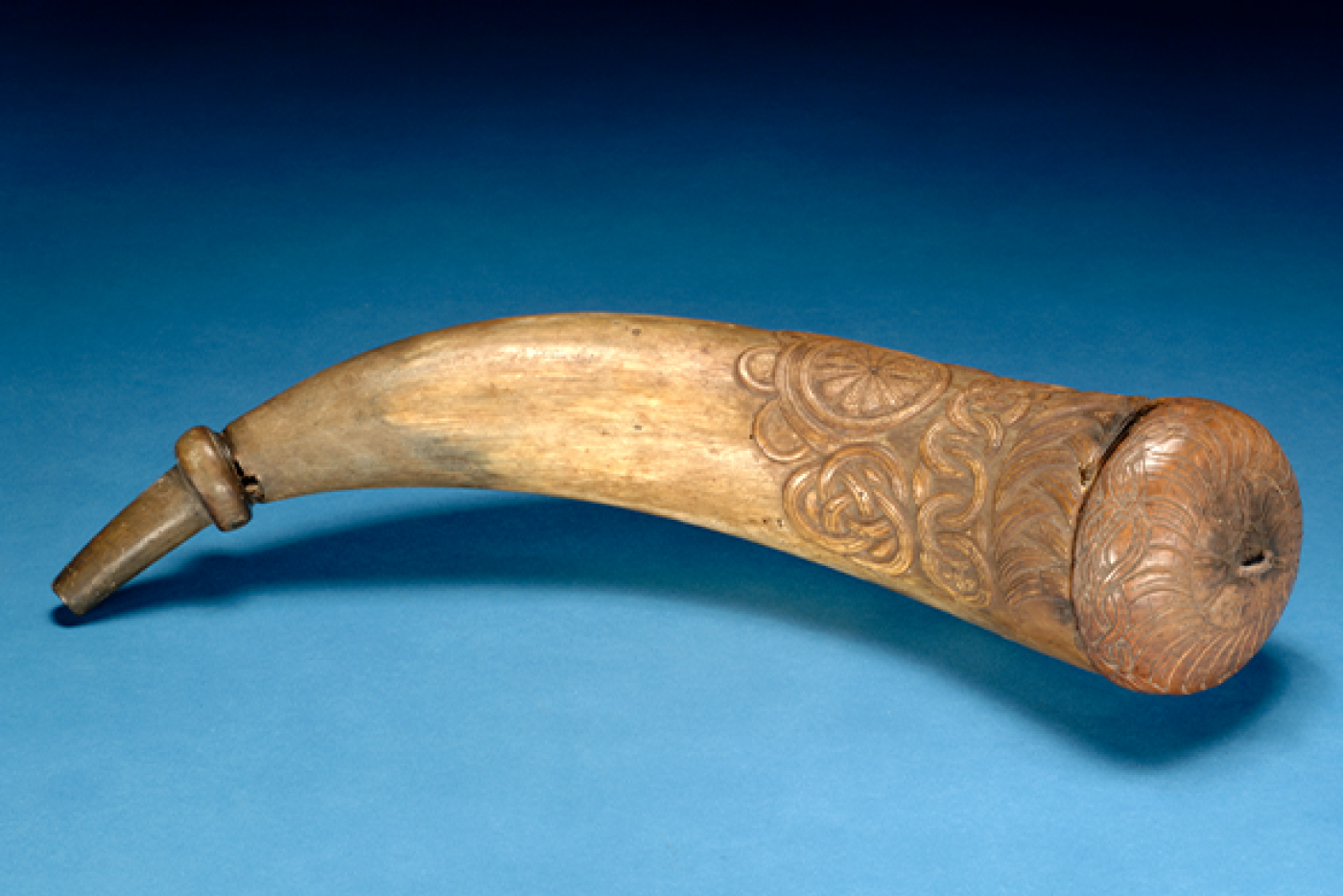 A tan horn with carved decorative patterns and a capped end over a blue background.
