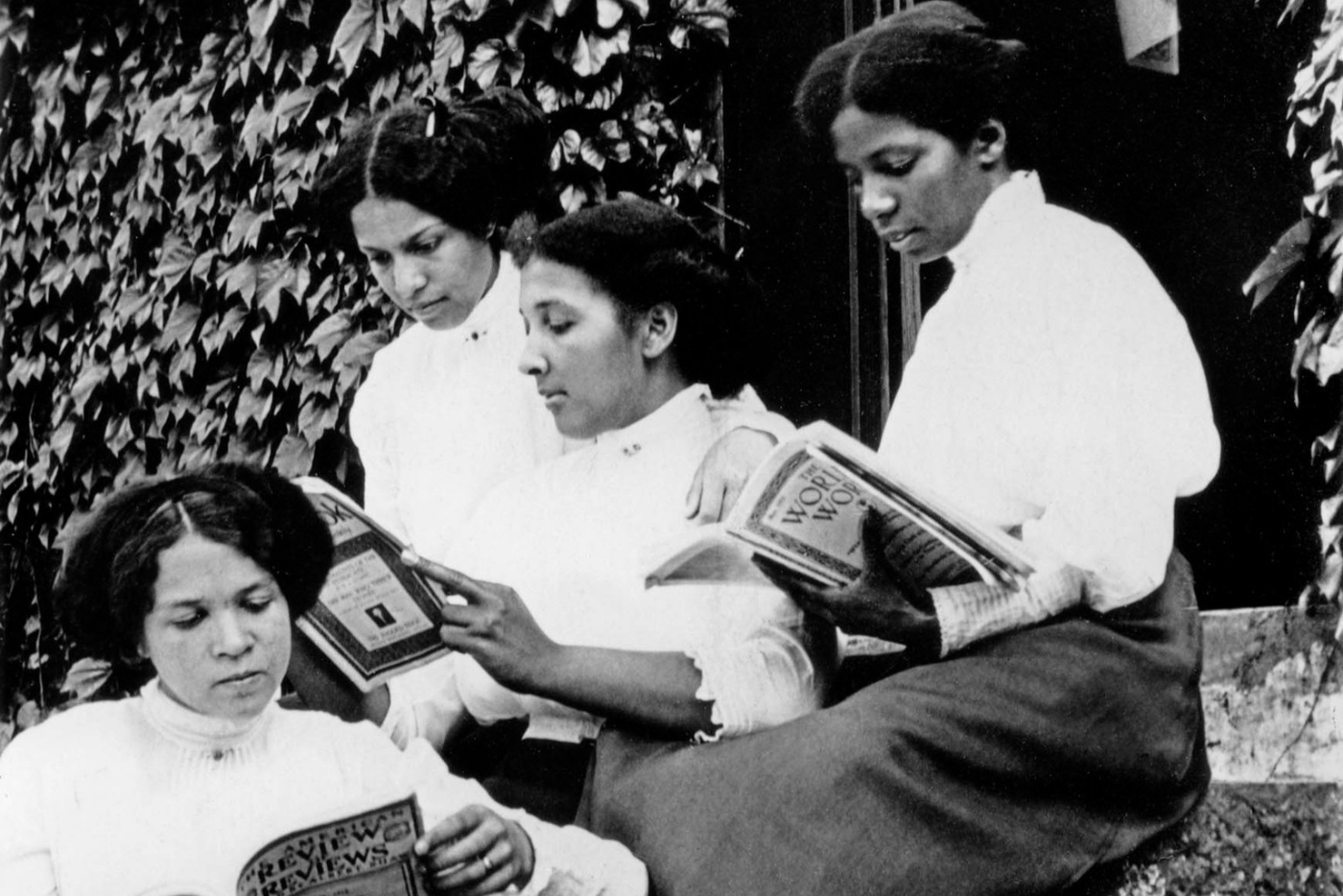 Black-and-white photograph of four women seated outdoors on stone steps, each reading a book.