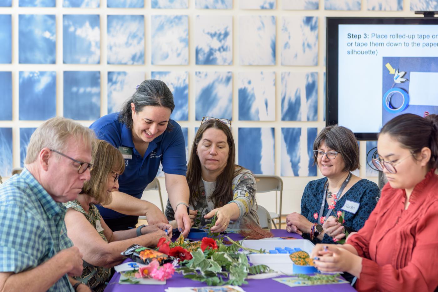 A group of women create colorful crafts around a table.
