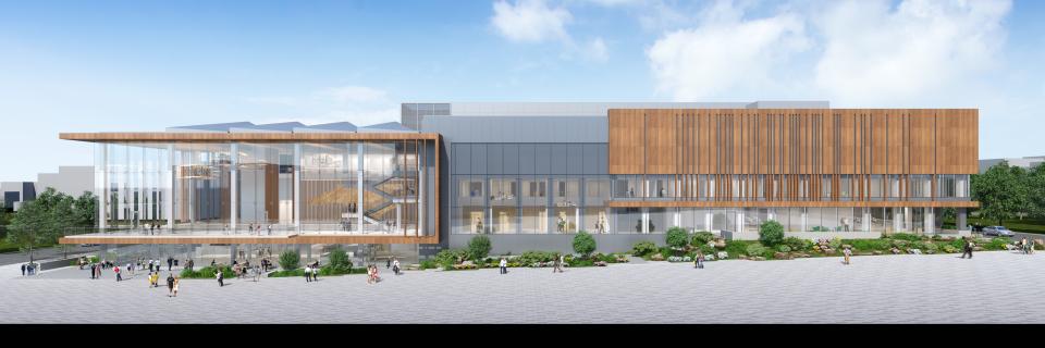 An architectural rendering of a wide, modern multi-story building featuring a large glass atrium on the left and a facade screened with warm wood louvers on the right. The design combines glass, grey concrete, and timber under a bright blue sky. A spacious light-grey plaza in the foreground is populated with small, scattered figures of people walking.