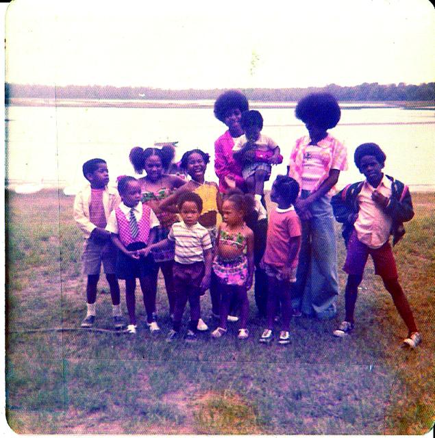 A vintage photo from the 70s of a group of cousins standing in front of a lake. 