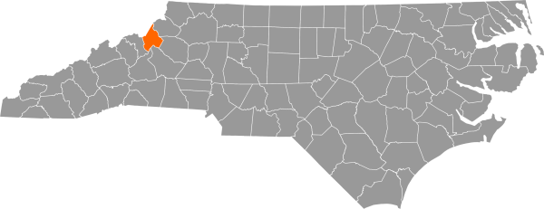 A gray map of North Carolina with Avery County filled in with orange.