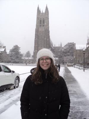 Hailey Kasney stands in front of Duke Chapel on a snowy day. She wears a white hat with a black jacket.