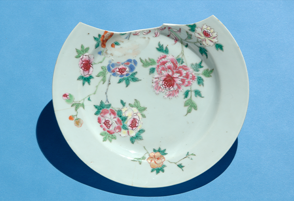 A white ceramic plate with a floral design and a chip at the top set against a blue background.