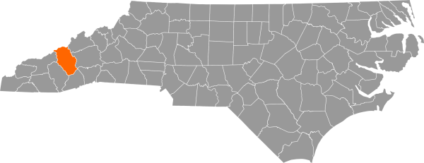 A gray map of North Carolina with Haywood County filled in with orange.