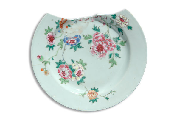 A white ceramic plate with a floral design and a chip at the top set against a blue background.