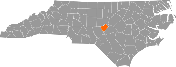 A gray map of North Carolina with Lee County filled in with orange.