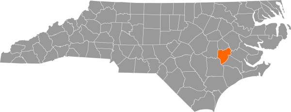 A gray map of North Carolina with Lenoir County filled in with orange.