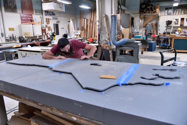 Man sands a large panel shaped like North Carolina in a workshop.