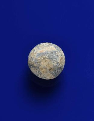 A grapeshot ball with a rough gray and tan surface on a blue background.
