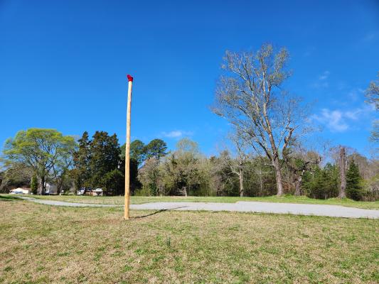 Hand-hewn wooden pole with a red cap standing in a grassy field at Historic Halifax under a clear blue sky.