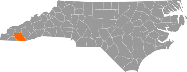 A gray map of North Carolina with Macon County filled in with orange.