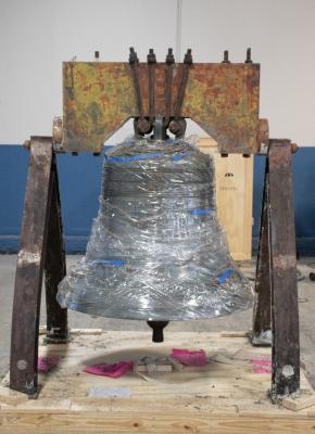 Liberty Bell replica wrapped in protective plastic during conservation treatment, mounted on a metal frame.