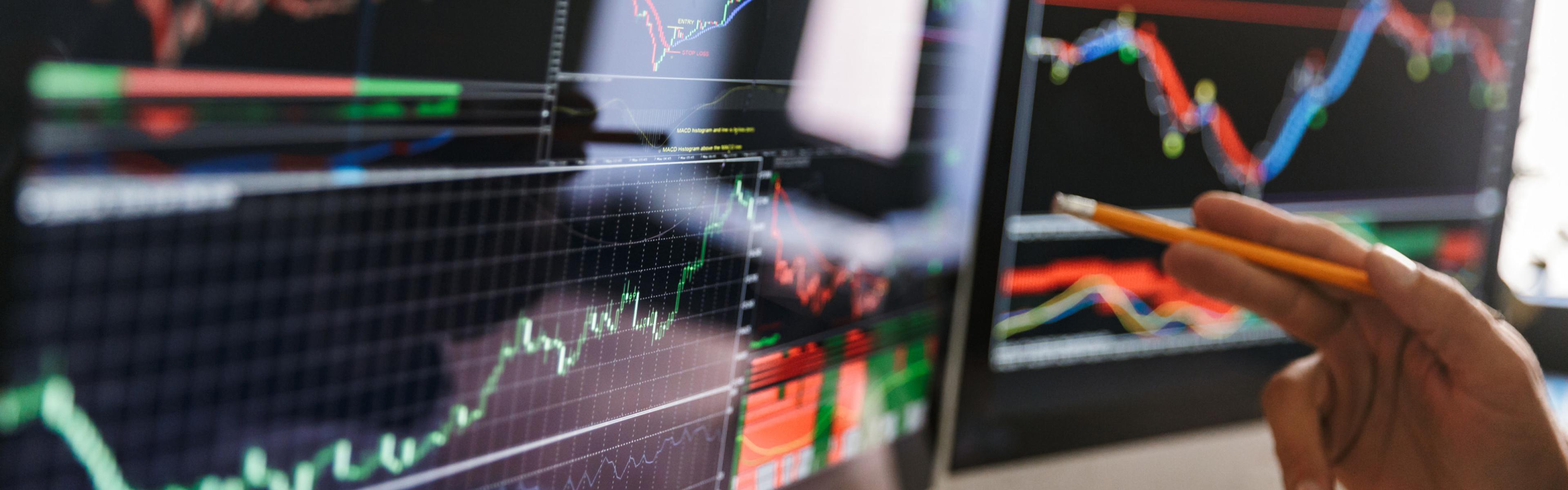 Person's hand pointing to a stock chart on a computer screen