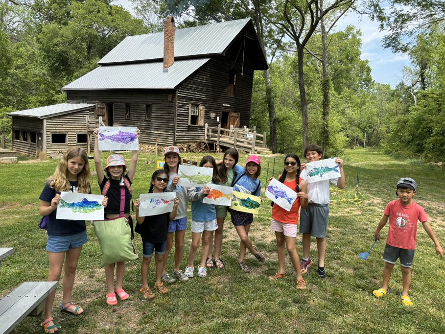 Elementary schoolers posing in front of cabin with fish paintings