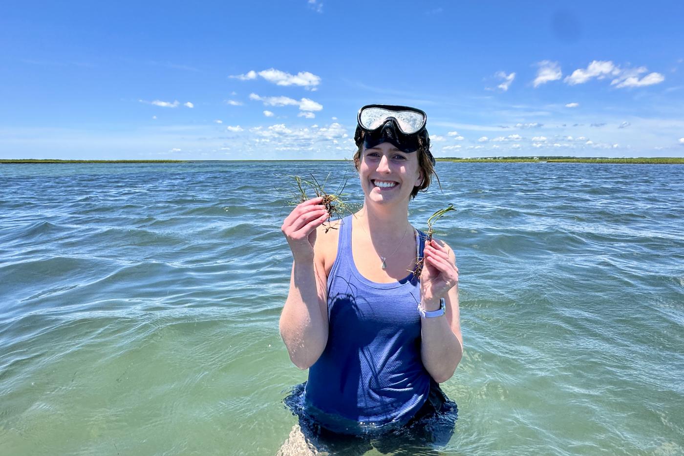 STEM Policy Fellow, Riley Ragain, holding up seagrass while standing in waist deep water. 