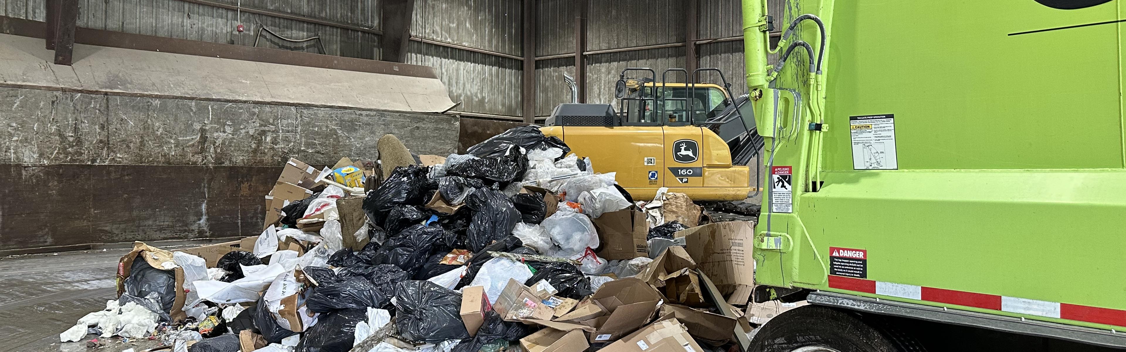 A green trash truck dumping recycling material in a warehouse. 