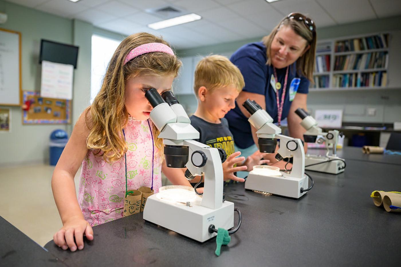 Two children looking through a microscope with a teacher looking on